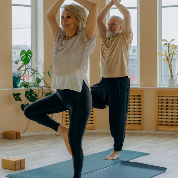 Smiling woman stretching gently in a sunlit room, embodying vitality.